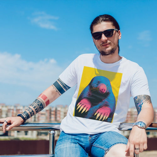 A man wearing a white graphic t-shirt with an Andy Warhol style Wry Bird print, blue denim shorts, and sunglasses, sitting outdoors against a blue sky background.