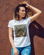A woman with curly hair wearing a white graphic Wry Bird t-shirt with a square owl print, paired with blue jeans, posing against a textured reddish-brown stucco wall.